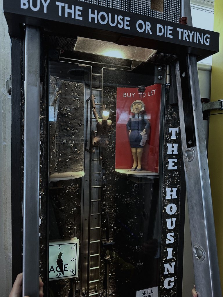 Set in a seaside amusement arcade and a semi-detached kitchen in a small English coastal town, because the mechanism needed somewhere ordinary and slightly faded to hide in.